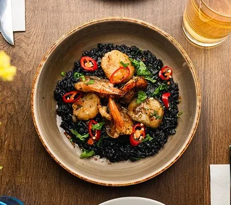 Venetian black squid ink risotto garnished with seared scallops and sautéed prawns